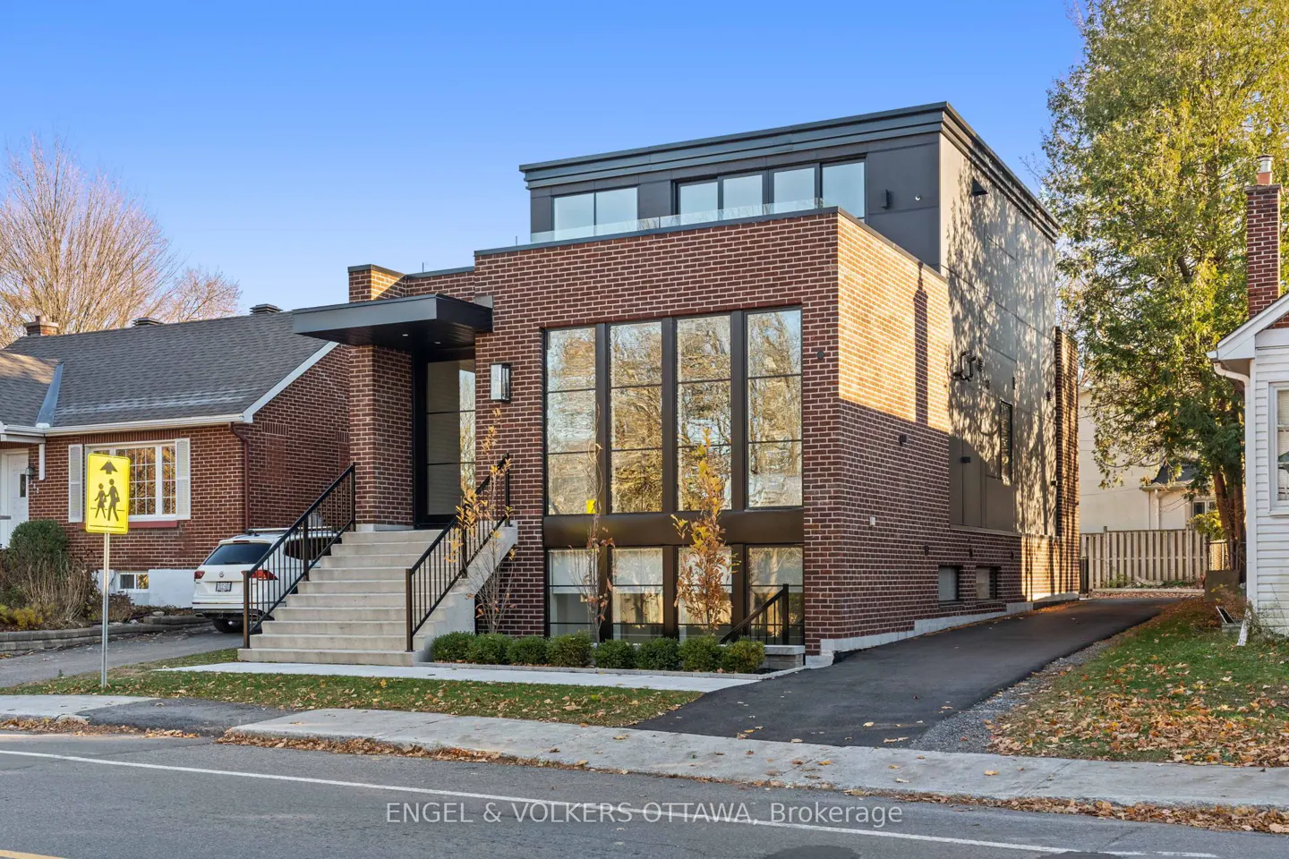 Modern brick house with large windows and a black trim. A set of stairs leads to the front door. A driveway is on the right side of the house.