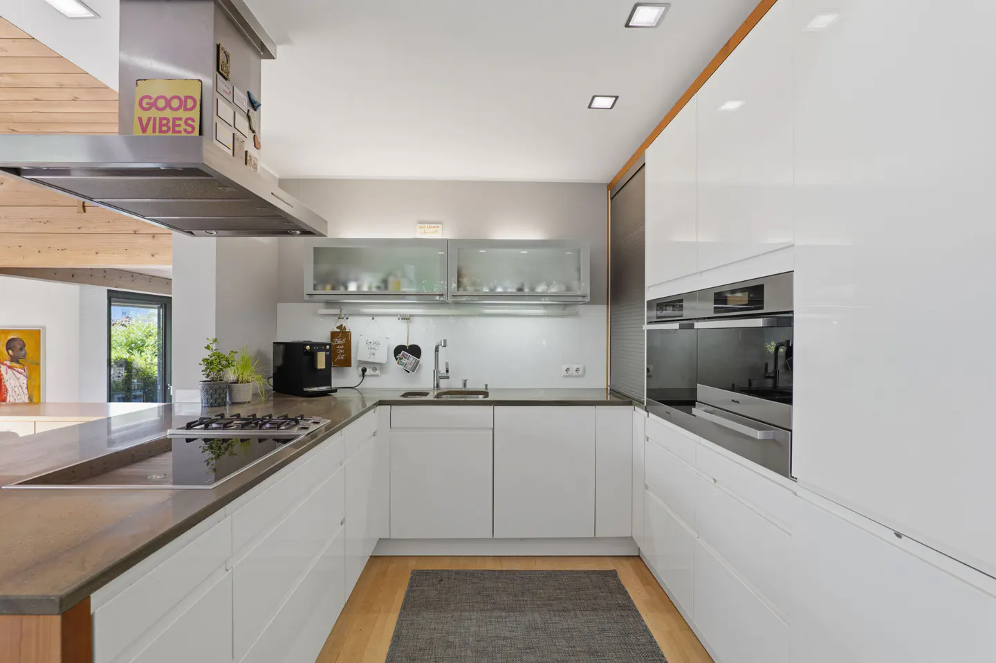 Modern U-shaped kitchen with white glossy cabinets, stainless steel appliances, dark countertops, and a grey floor rug.