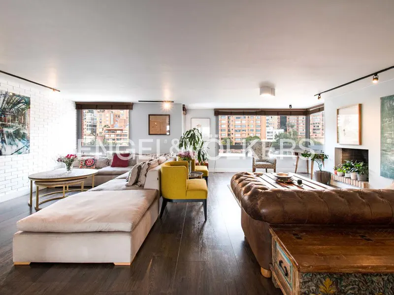 Wide shot of a living room with a beige sectional, yellow chairs, and a brown leather sofa. Windows overlook a city.