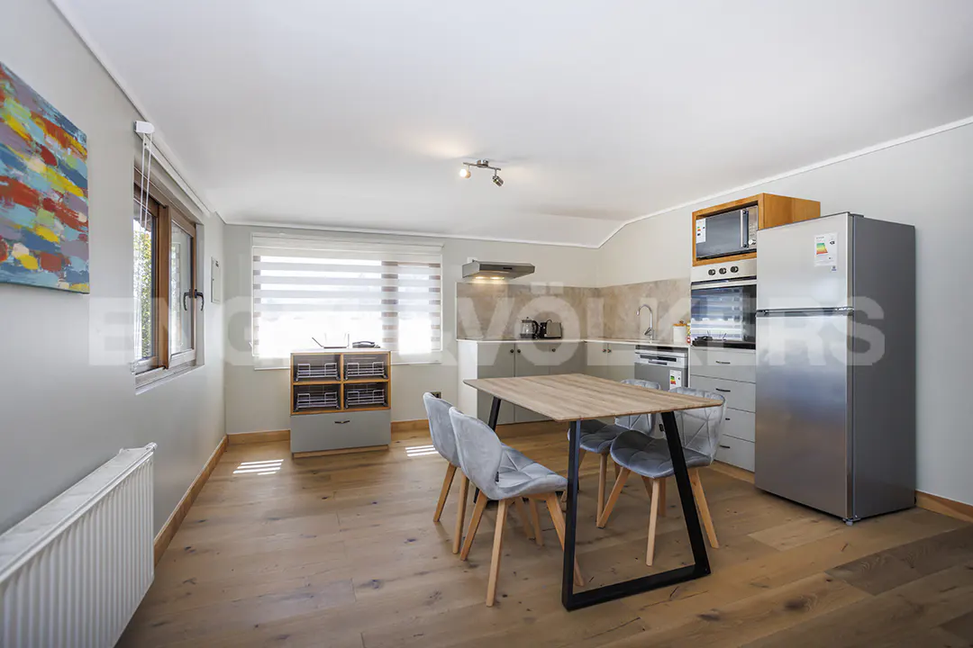 Open-concept kitchen and dining area with wood floors, gray cabinets, and a stainless steel refrigerator. A wooden table with four gray chairs sits in the center.