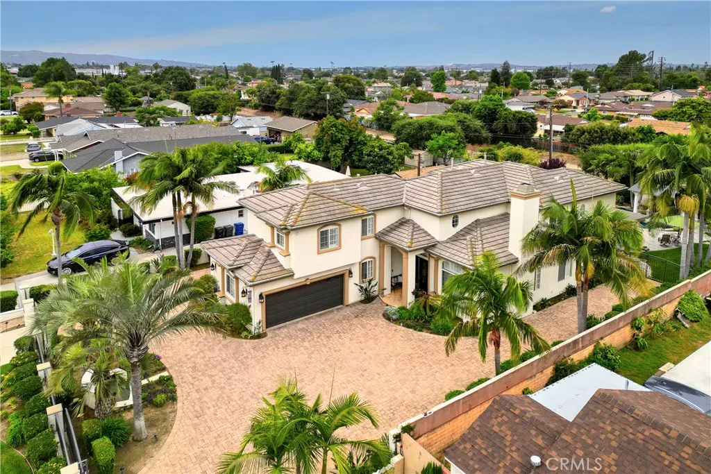 Aerial view of a two-story beige house with a brown roof, surrounded by palm trees and a brick driveway.