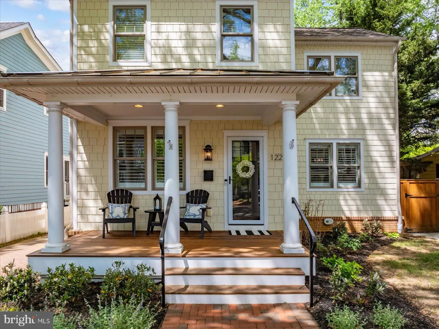Two-story house with yellow siding, white trim, and a front porch with two black chairs. The house number "122" is visible above the door.
