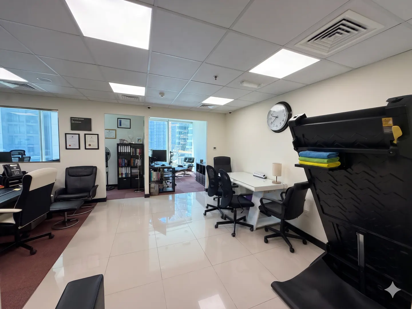 Bright office space with white tile floors, a white table with black chairs, and a black clock on the wall.