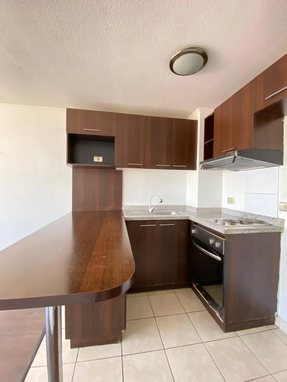 A kitchen with dark wood cabinets, granite countertops, and tile flooring. A large wooden table extends into the room.