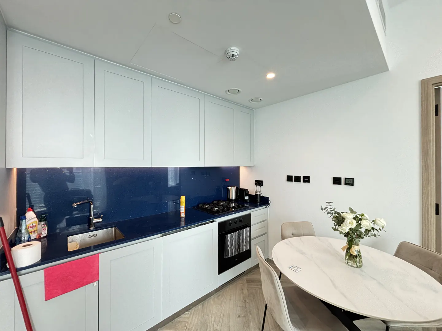 A modern kitchen with light blue cabinets, a dark blue countertop, and a white marble dining table with chairs.