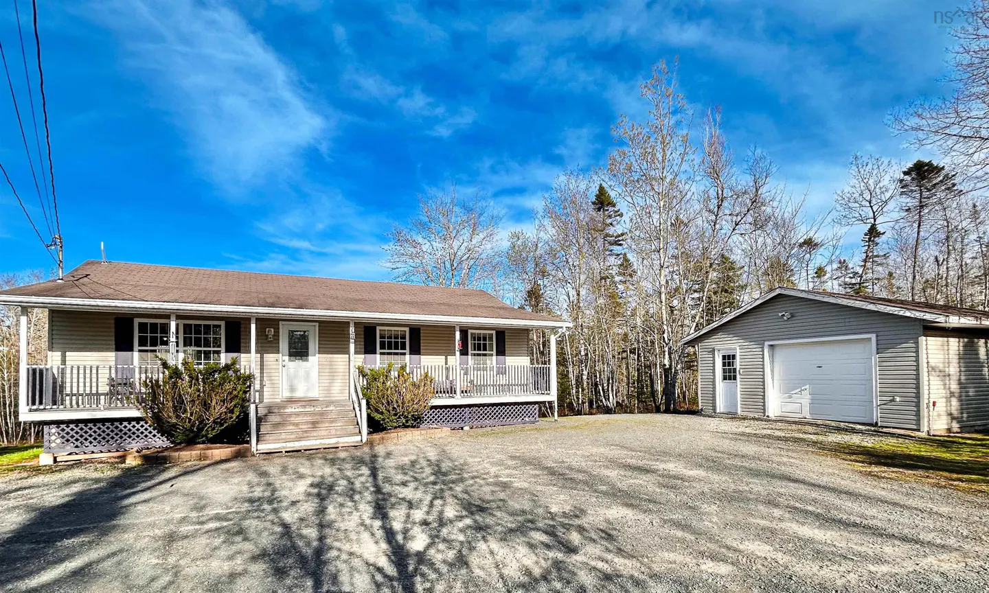 A tan ranch-style house with a brown roof and a gray detached garage on a gravel driveway.