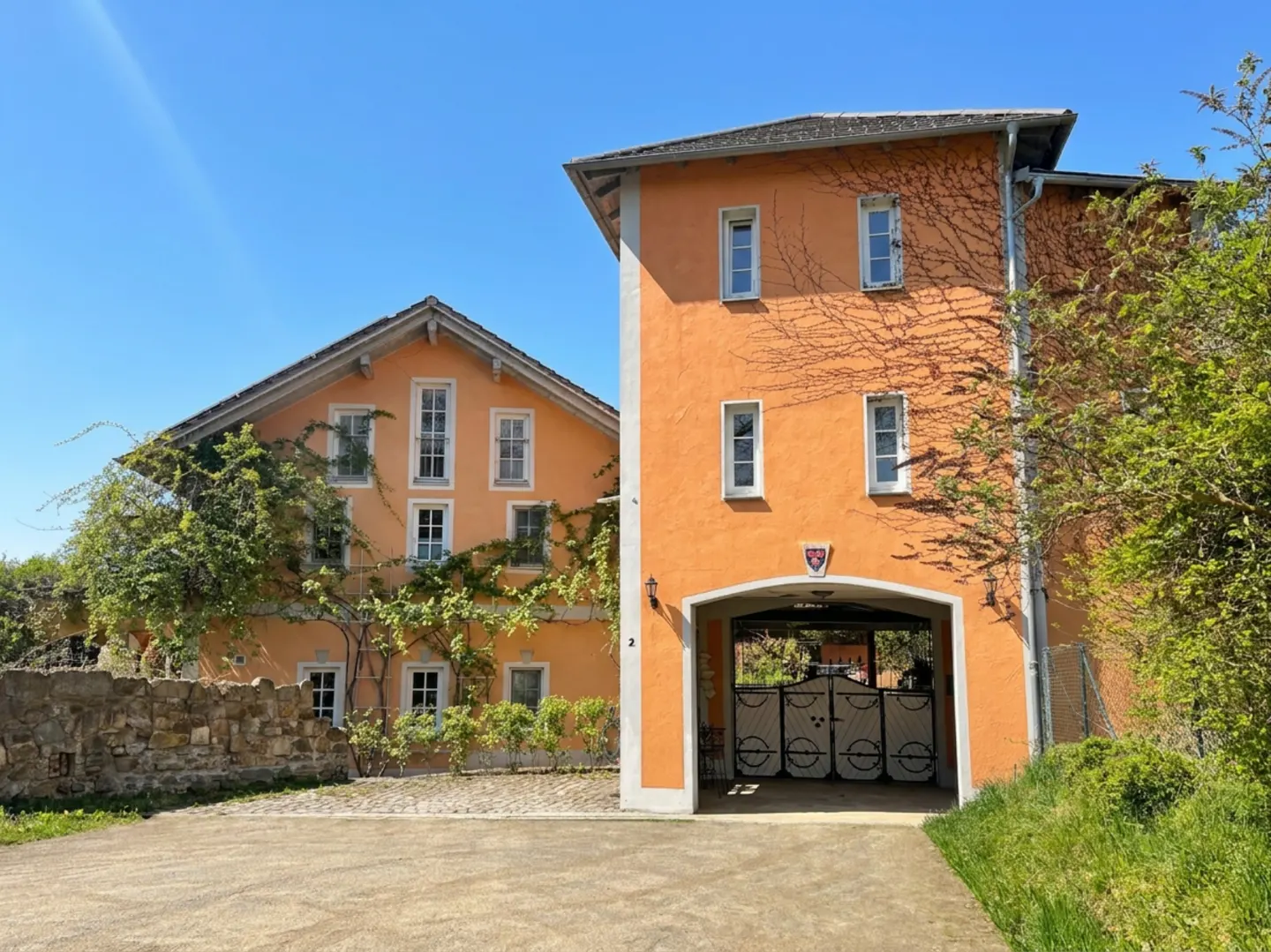 Orange two-story house with white windows and a gated entrance. Vines climb the walls under a clear blue sky.