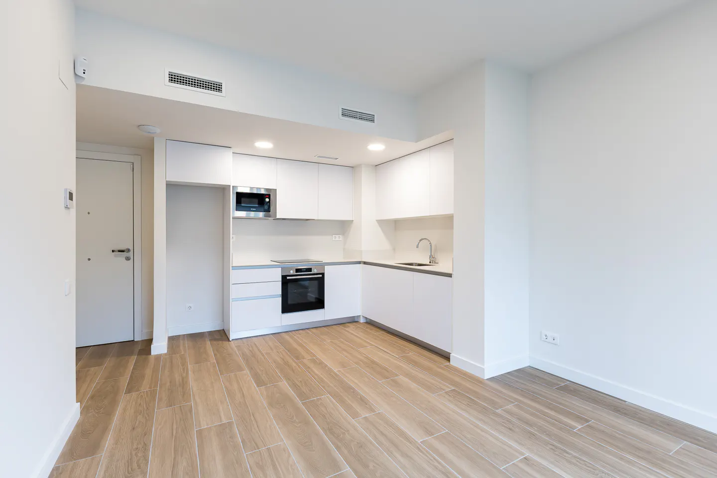 Bright, modern kitchen with white cabinets, stainless steel appliances, and wood-look tile flooring in an open-concept space.