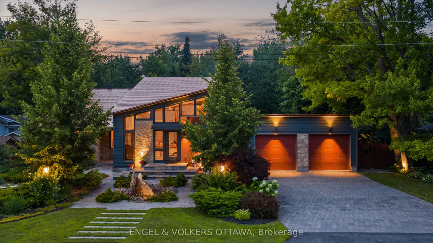 A modern home with a stone and blue facade, large windows, and a red garage door is surrounded by lush greenery.