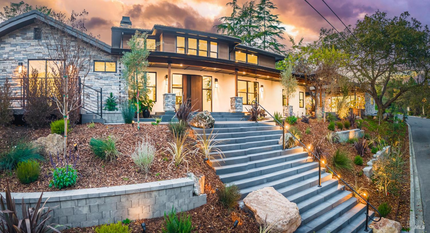 Modern home with stone facade and wide stairs leading to the front door, set against a vibrant sunset sky.