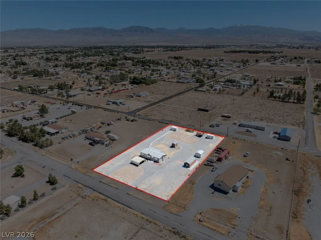 Aerial view of a property outlined in red, featuring a mobile home, outbuildings, and a large lot in a rural setting with mountains in the distance.