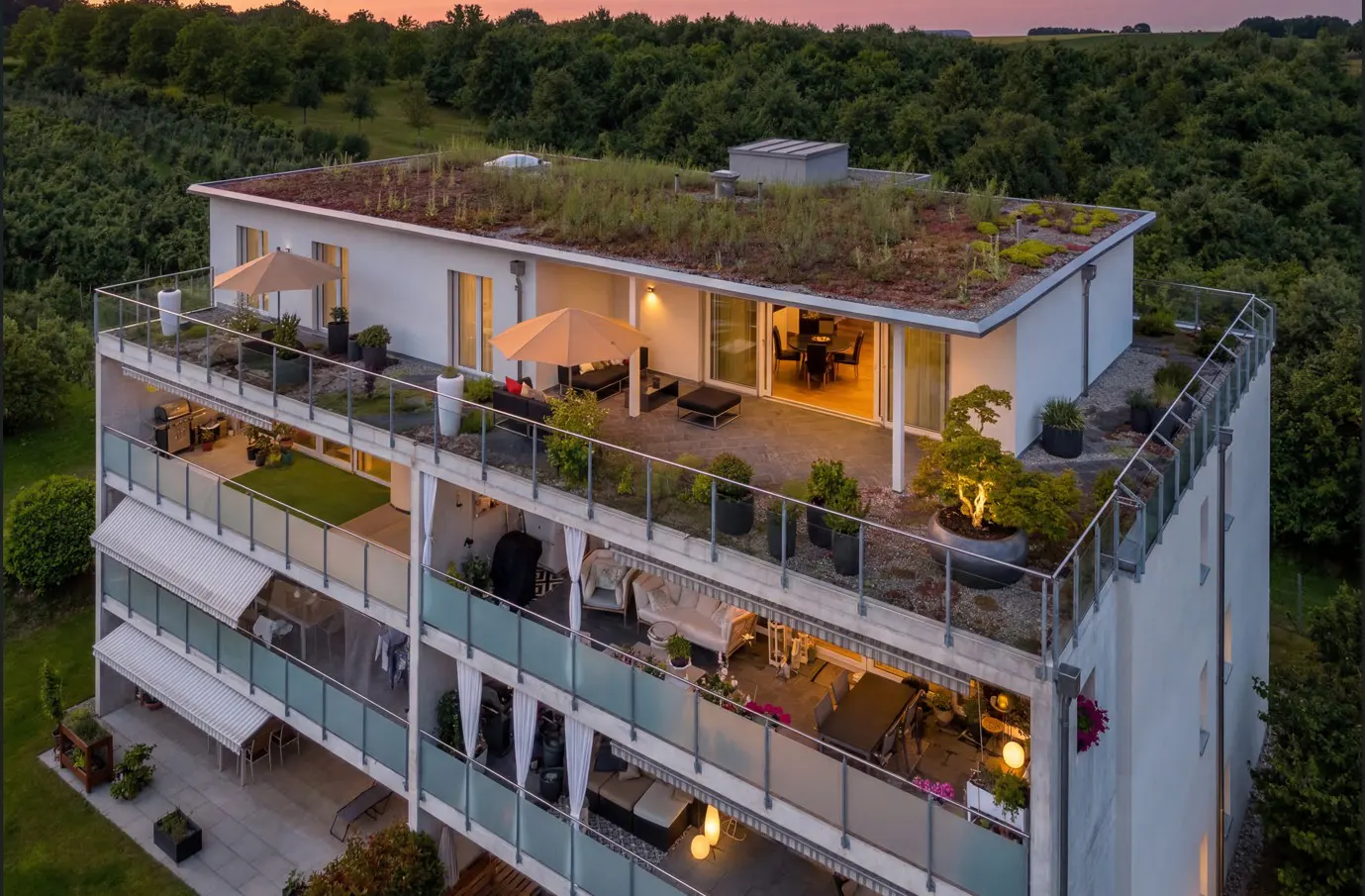 Exterior view of a modern apartment building with balconies and a green roof, surrounded by trees.