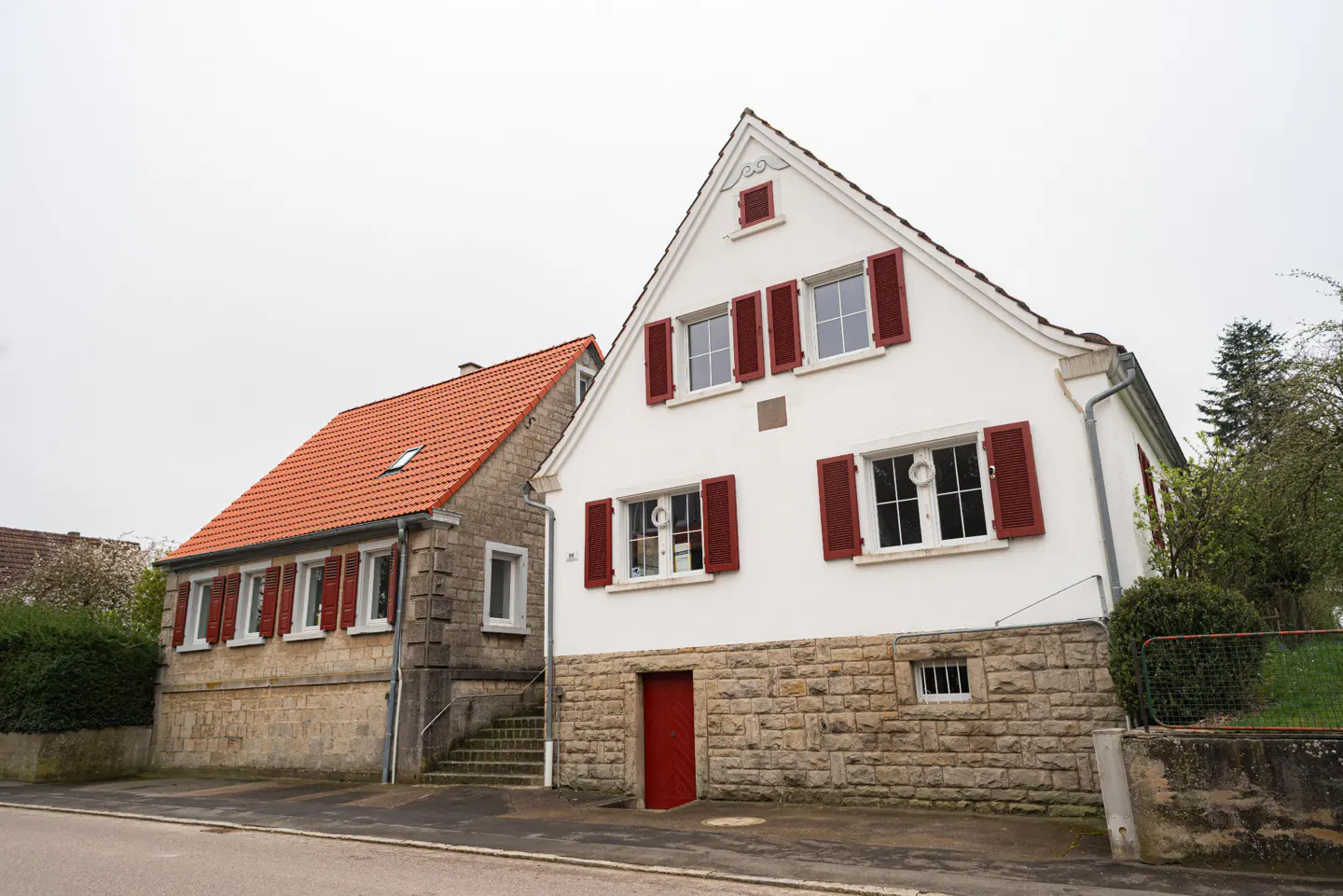 Two-story houses with red shutters and roofs. One is white, the other is stone.