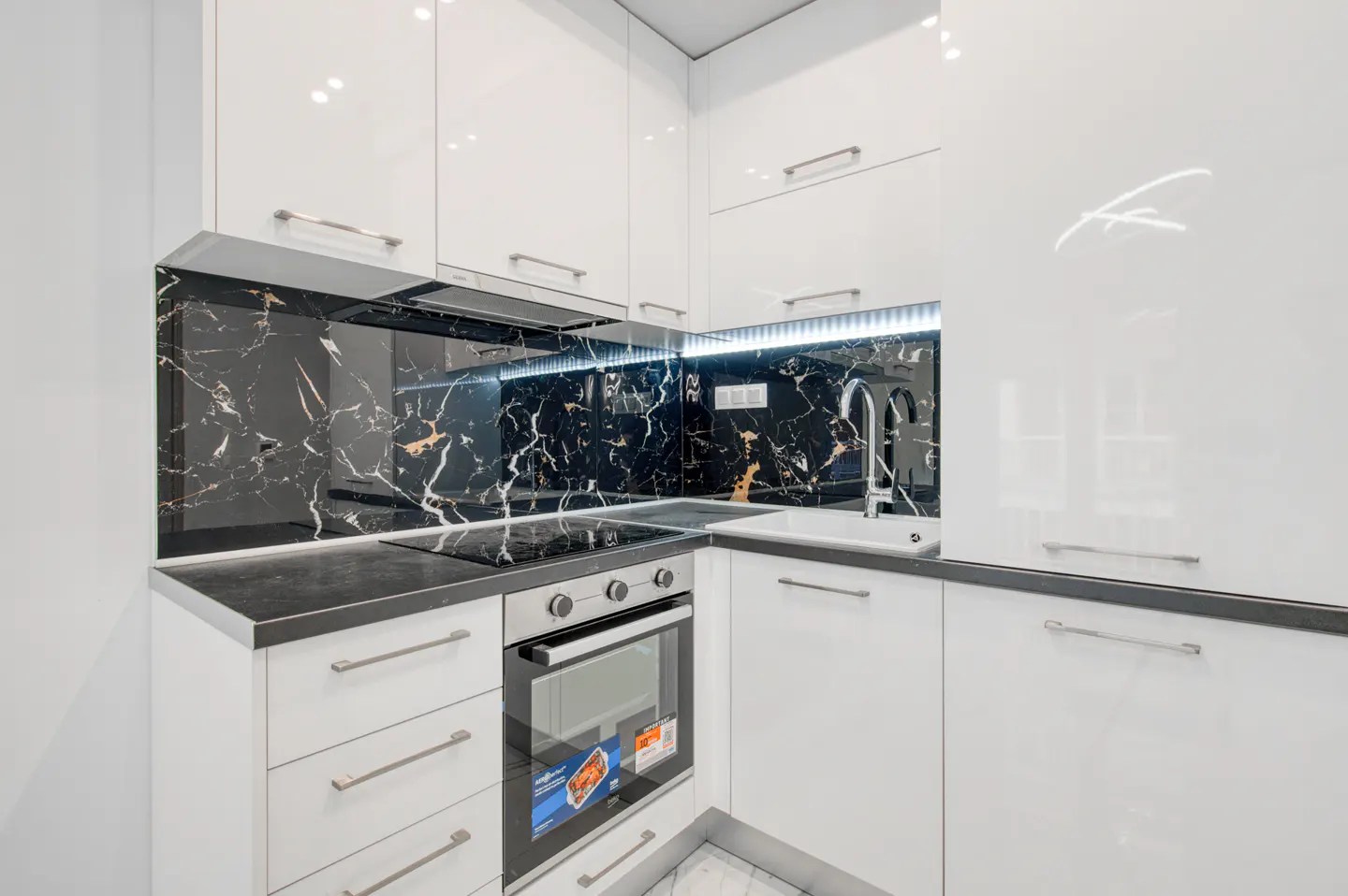 A modern kitchen with white cabinets, black marble backsplash, and stainless steel appliances.