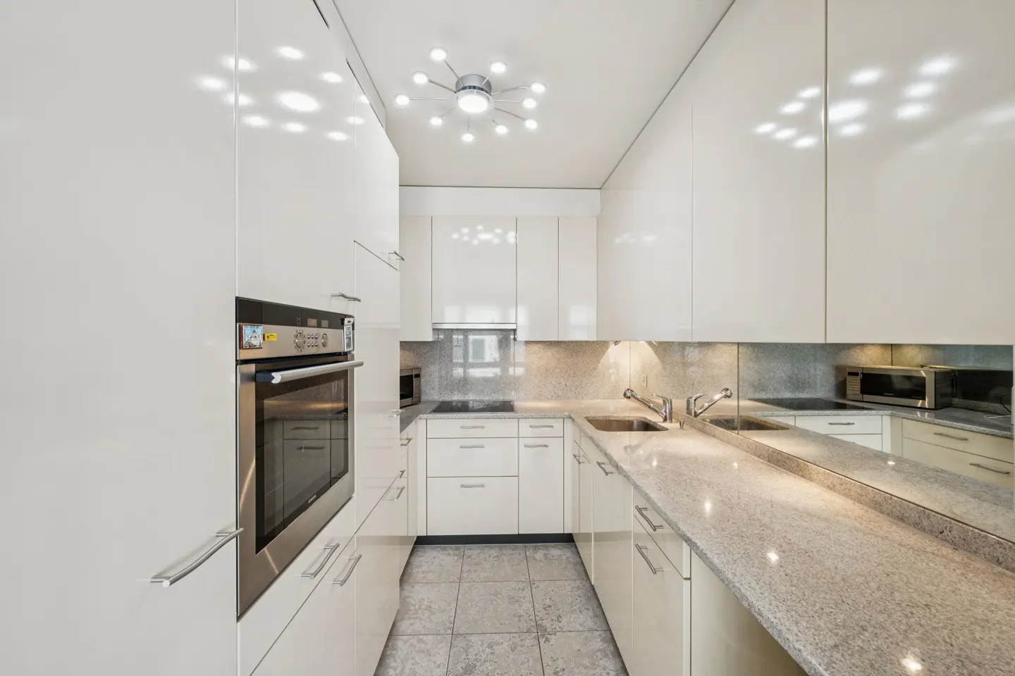 A modern kitchen with white cabinets, stainless steel appliances, and granite countertops. A unique light fixture illuminates the space.