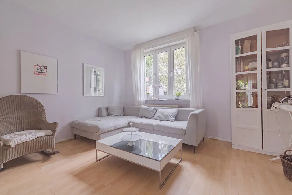 Bright living room with light gray walls, a sectional sofa, a wicker rocking chair, and a modern white coffee table.