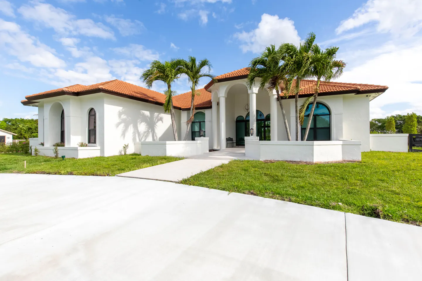 Front view of a white, single-story house with a red tile roof and palm trees.