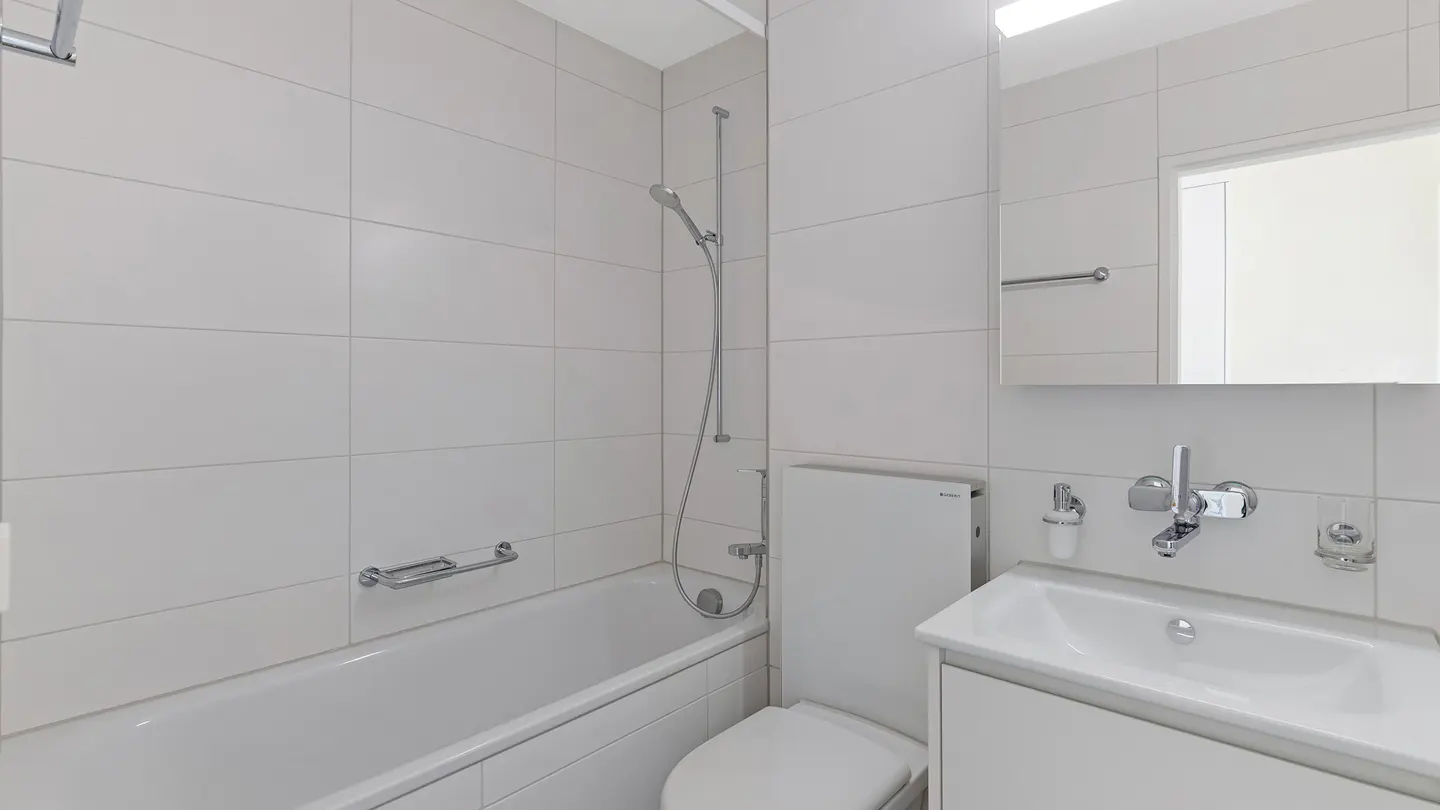 Bright, modern bathroom with white tile, a bathtub with shower, toilet, and sink with vanity.
