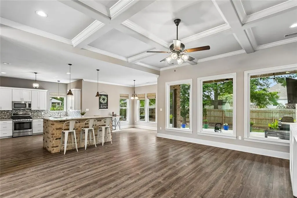 Open-concept kitchen and living room with hardwood floors, white cabinets, brick island, and large windows overlooking the backyard.