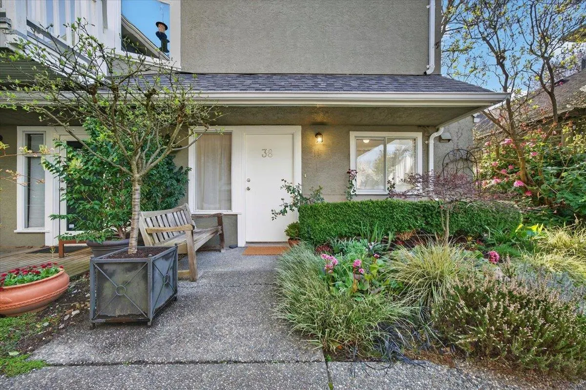 Exterior of a gray townhouse with a white door numbered 38, a bench, and a garden.