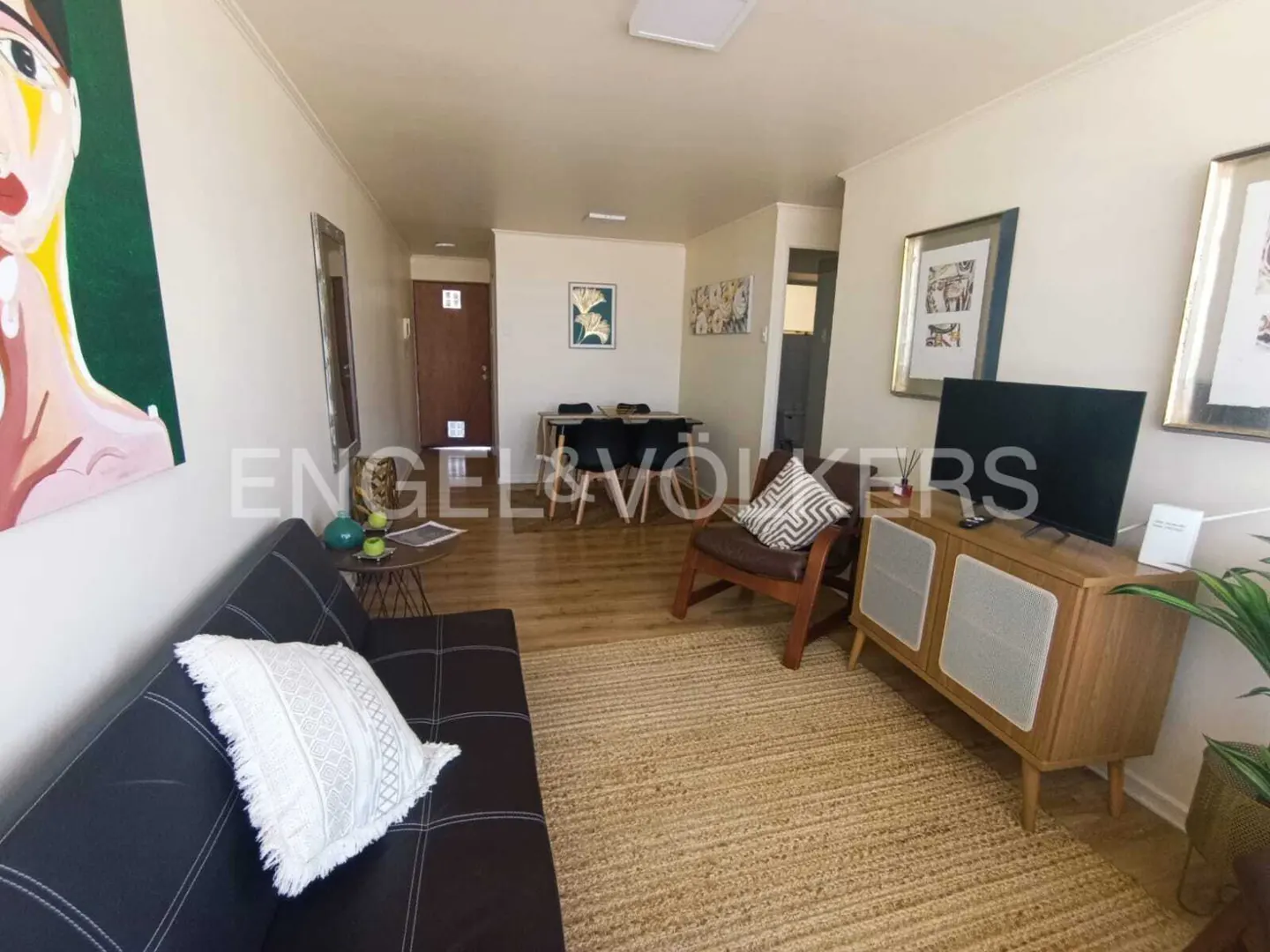 Living room with a black sofa, brown chair, TV on a wooden cabinet, and a dining table in the background.