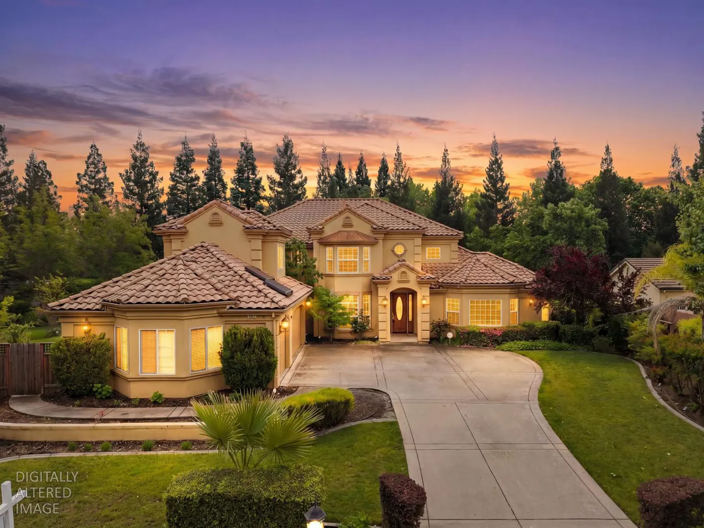 Two-story tan house with a red tile roof, a concrete driveway, and green grass at sunset.
