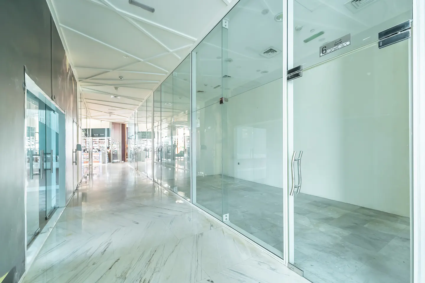 Hallway with glass-walled offices and marble floors. A gym is visible in the background.