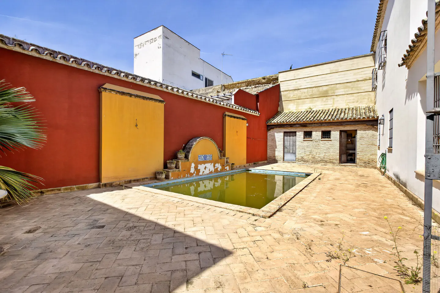 Courtyard with a rectangular pool, brick floor, and colorful walls. The walls are red and yellow, with a blue-tiled fountain.