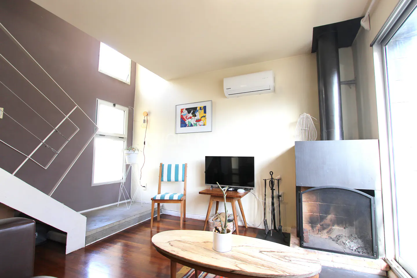 Living room with a fireplace, TV, and a blue and white striped chair. A modern staircase is on the left.
