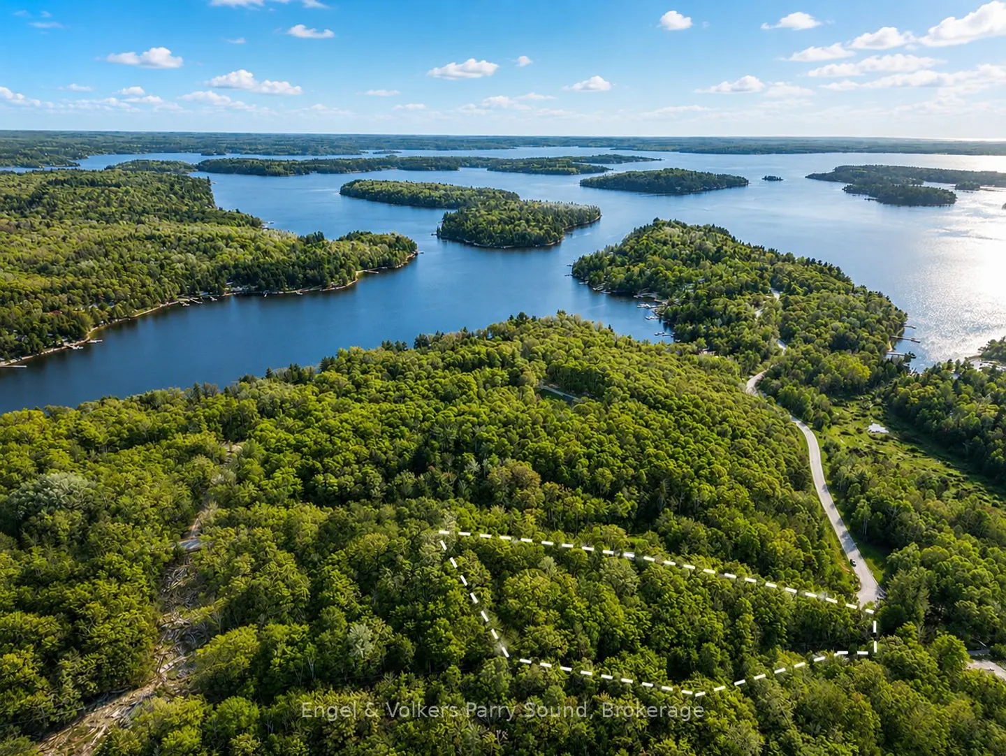 Aerial view of wooded land for sale, outlined in white, near a lake with islands under a blue sky.
