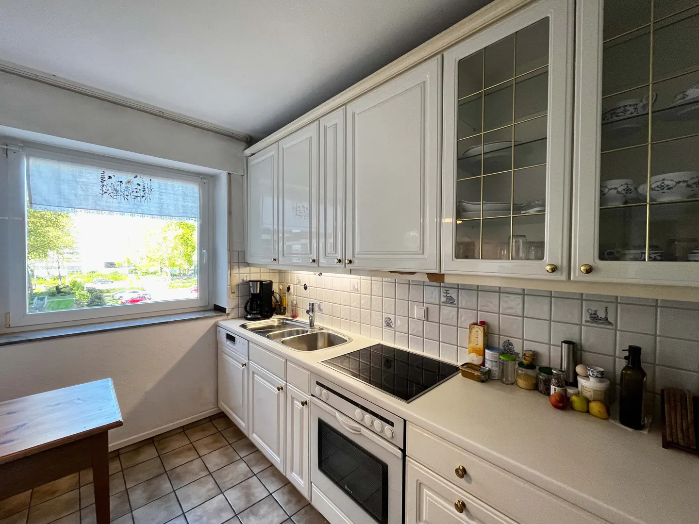 Bright kitchen with white cabinets, tiled backsplash, and a window showing a green outdoor view. Appliances and countertop items are visible.