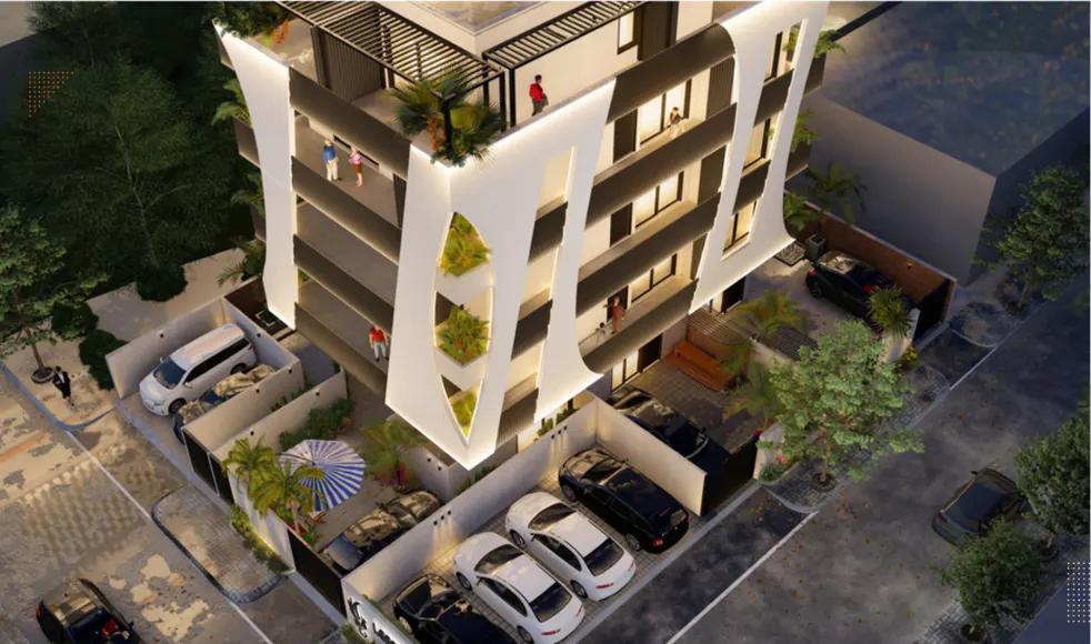 Aerial view of a modern white apartment building with balconies, parking spaces, and lush greenery. People are visible on the balconies and rooftop.