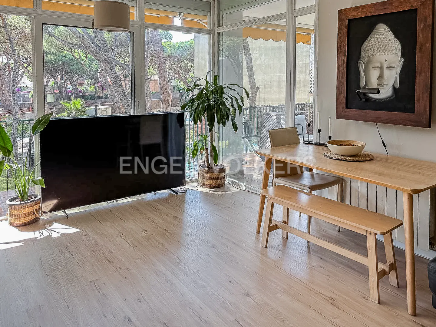 Living room with light wood floors, a dining table with bench, a large TV, and a Buddha portrait on the wall.