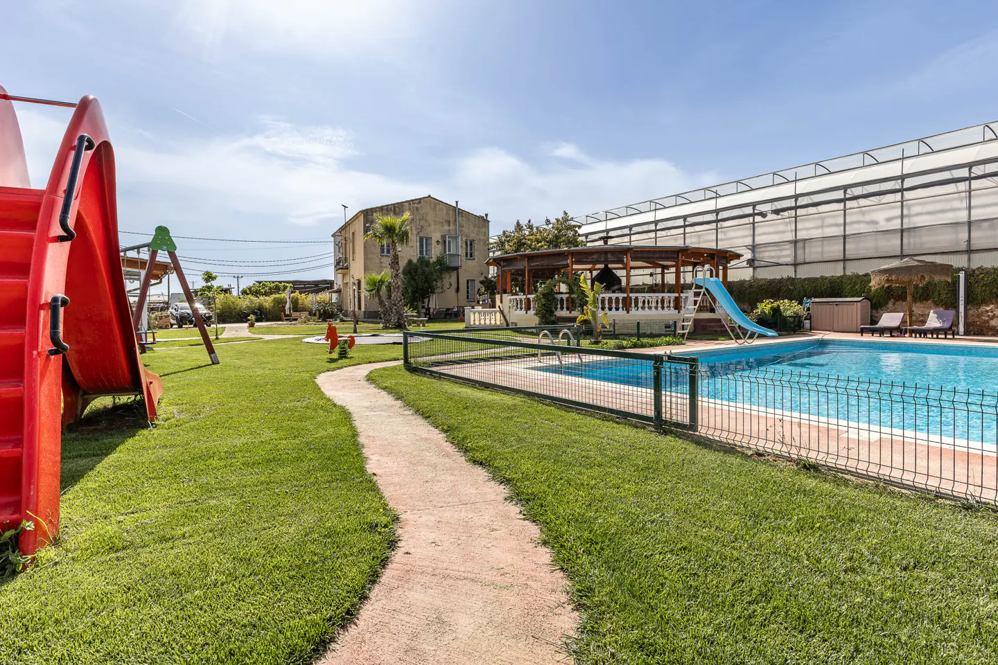 Outdoor shot of a property with a pool, playground, and a path leading to a building.