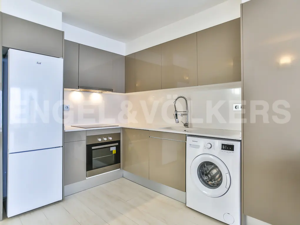 A modern kitchen with beige cabinets, a white refrigerator, oven, sink, and a washing machine.