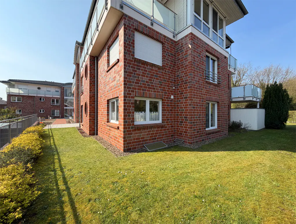 Exterior view of a red brick apartment building with white windows and a green lawn on a sunny day.