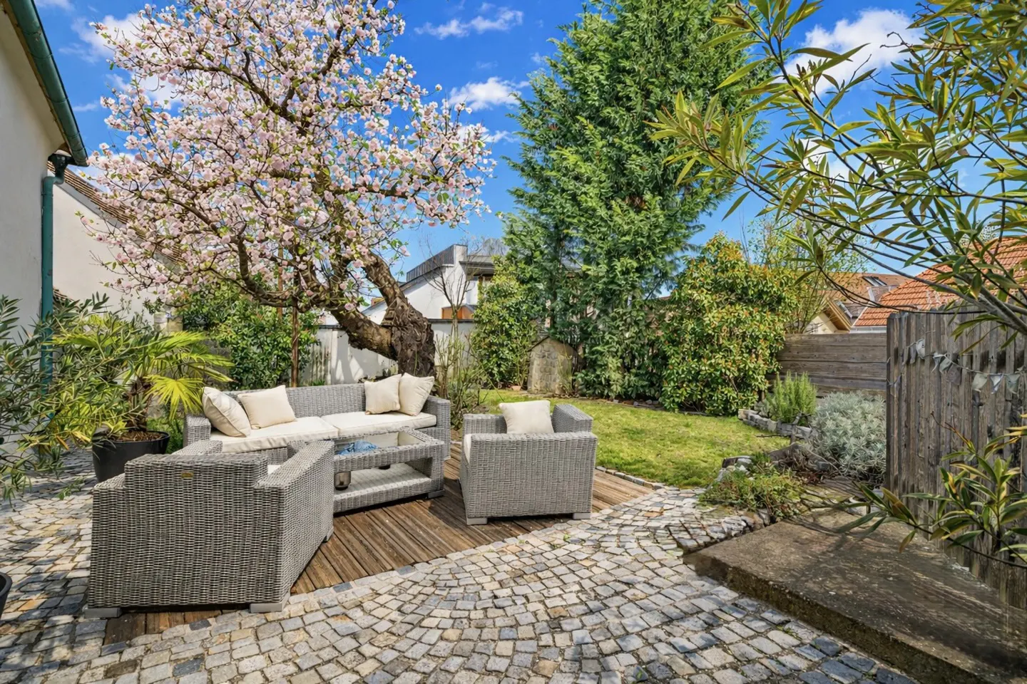 Outdoor patio with gray wicker furniture, a glass table, and a blooming cherry tree under a blue sky.
