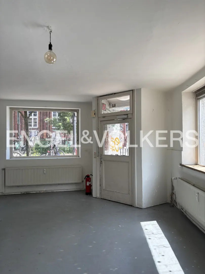 Empty commercial space with white walls, gray floors, large windows, a glass door, and a red fire extinguisher.