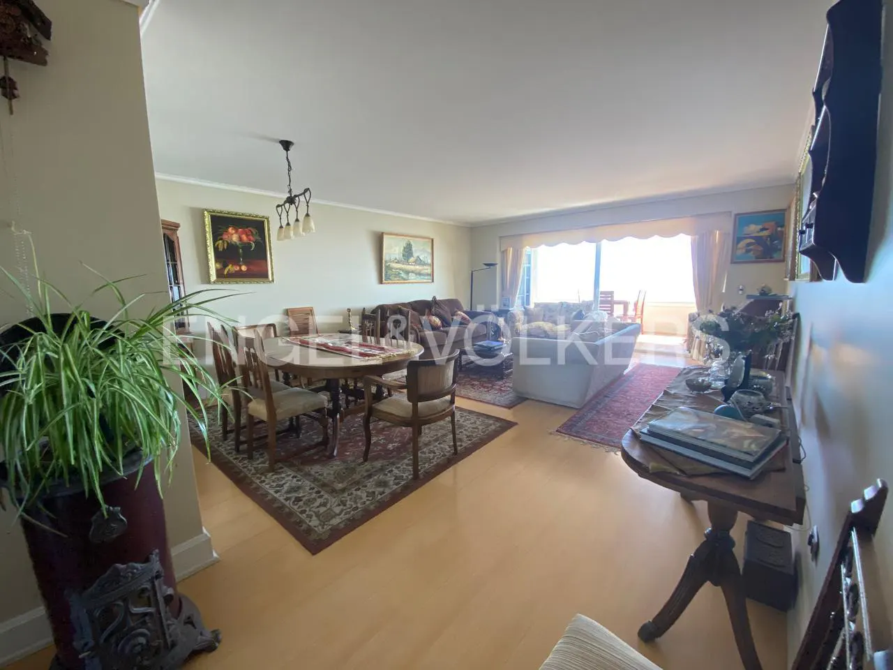 A bright living room with a dining table, sofas, and a view of the sea through a large window.