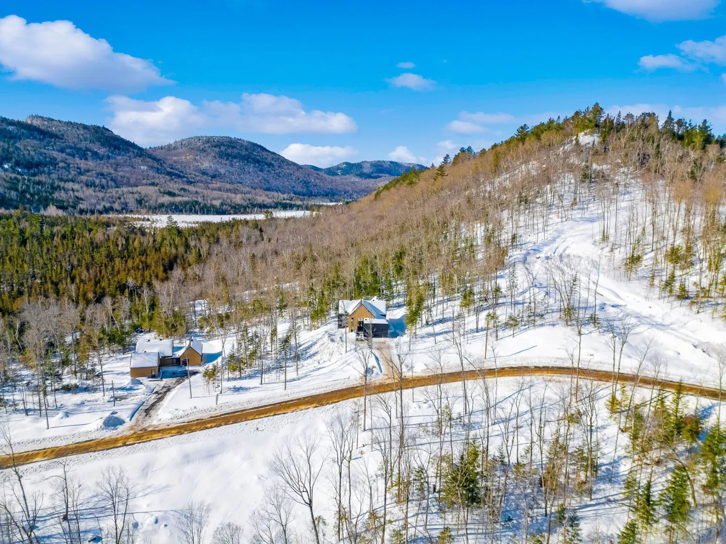 Aerial view of two modern homes in a snowy, wooded mountain landscape under a blue sky.