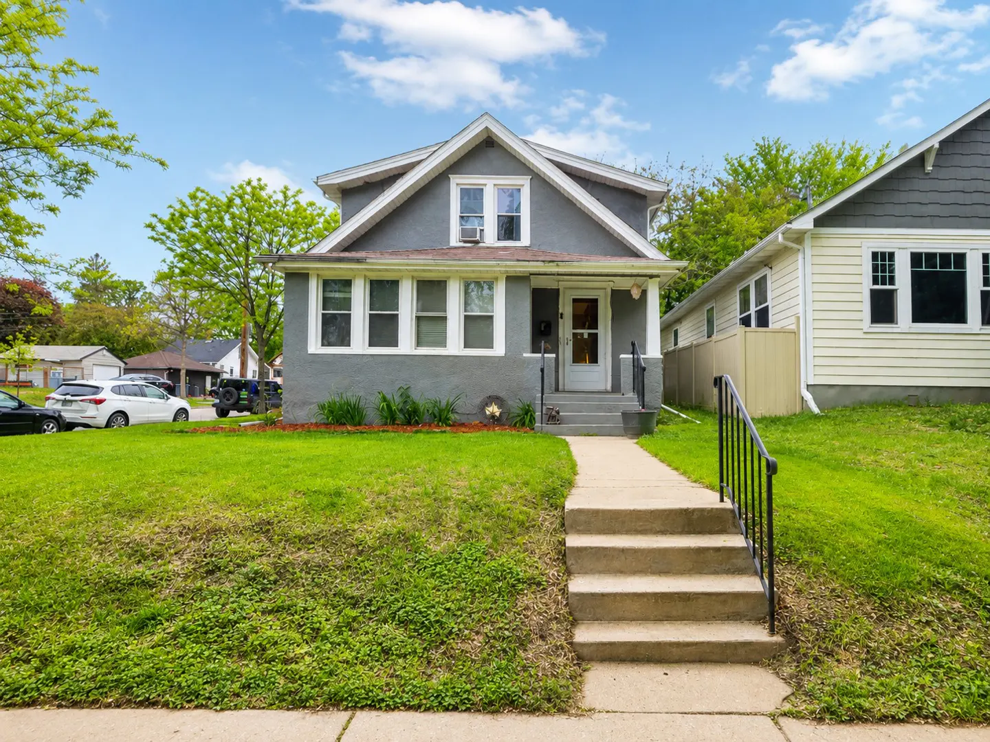 A gray two-story house with white trim and a concrete walkway leading to the front door. Green lawn and blue sky.