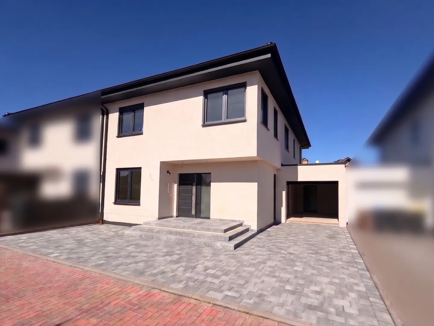 Two-story beige house with gray trim, windows, and door. Gray brick driveway and blue sky.