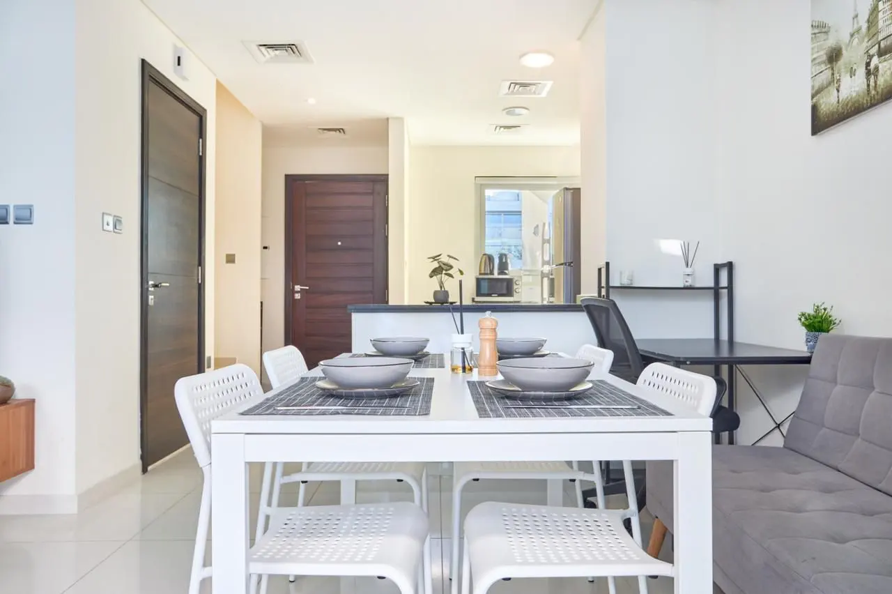 Bright apartment interior with a white dining table set for four, a gray sofa, and a black desk.
