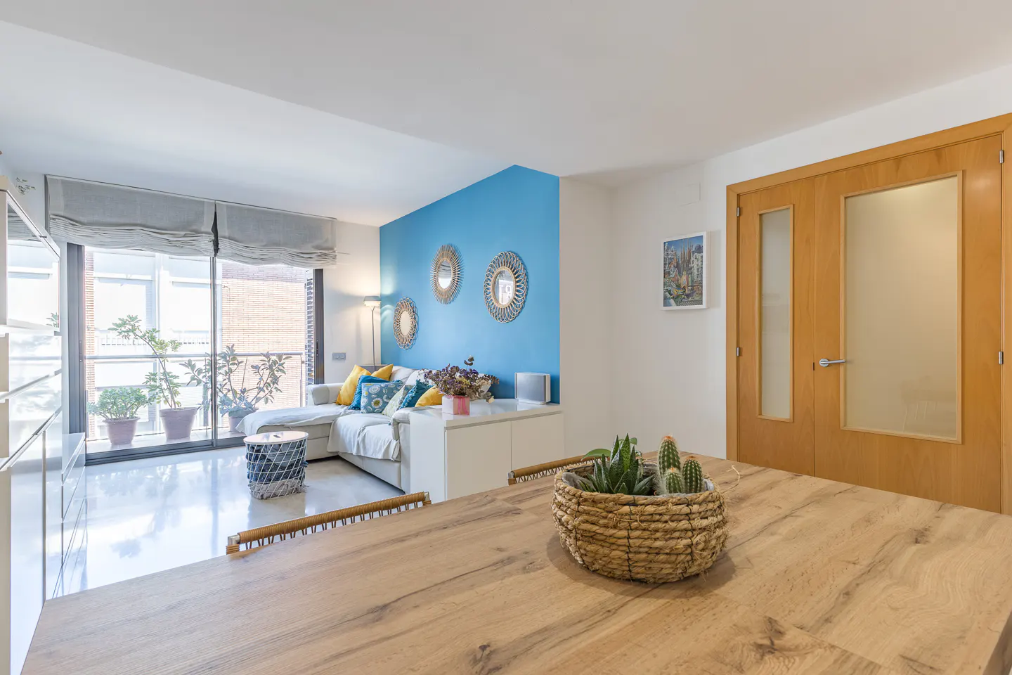 Bright living room with blue accent wall, white sofa, and wood table with a basket of succulents in the foreground.