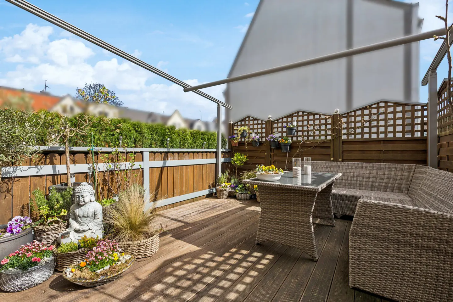 Outdoor patio with wooden deck, wicker furniture, and a Buddha statue surrounded by potted plants.