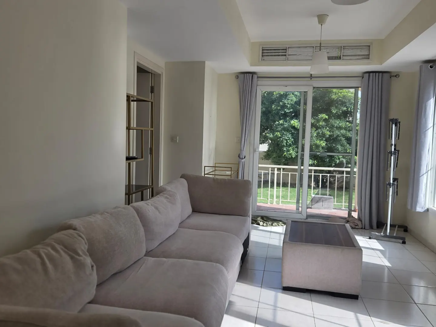 Living room with a beige sofa, coffee table, and sliding glass doors to a balcony with a green view.