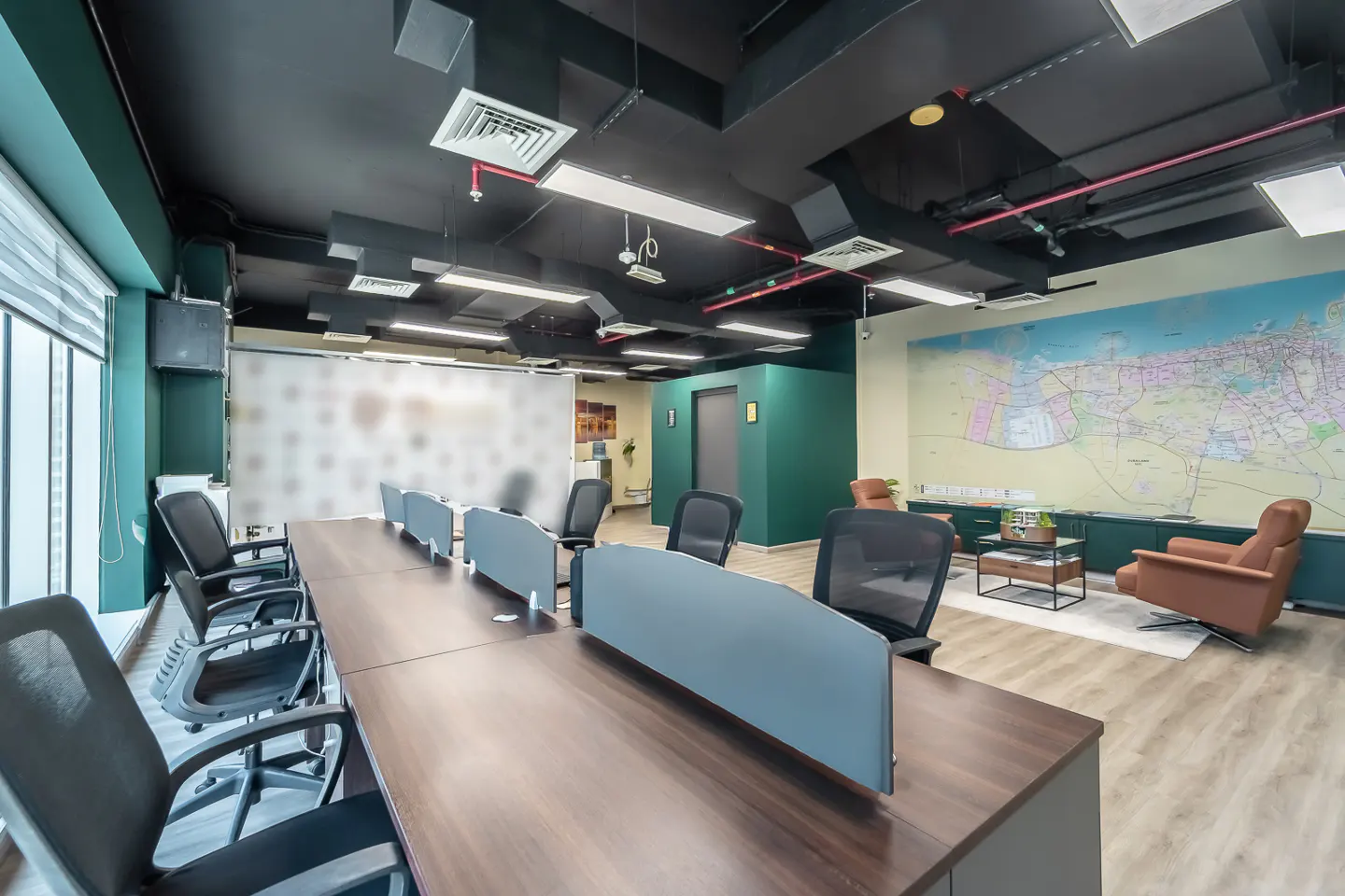 A modern office space with a long wooden table, black chairs, and a large map on the wall. The room has a black ceiling and green accents.