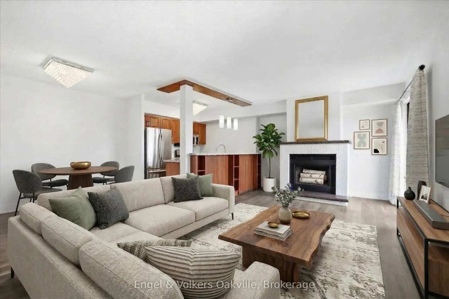 Open-concept living room with beige sectional, live-edge wood coffee table, fireplace, and dining area with wood cabinets.
