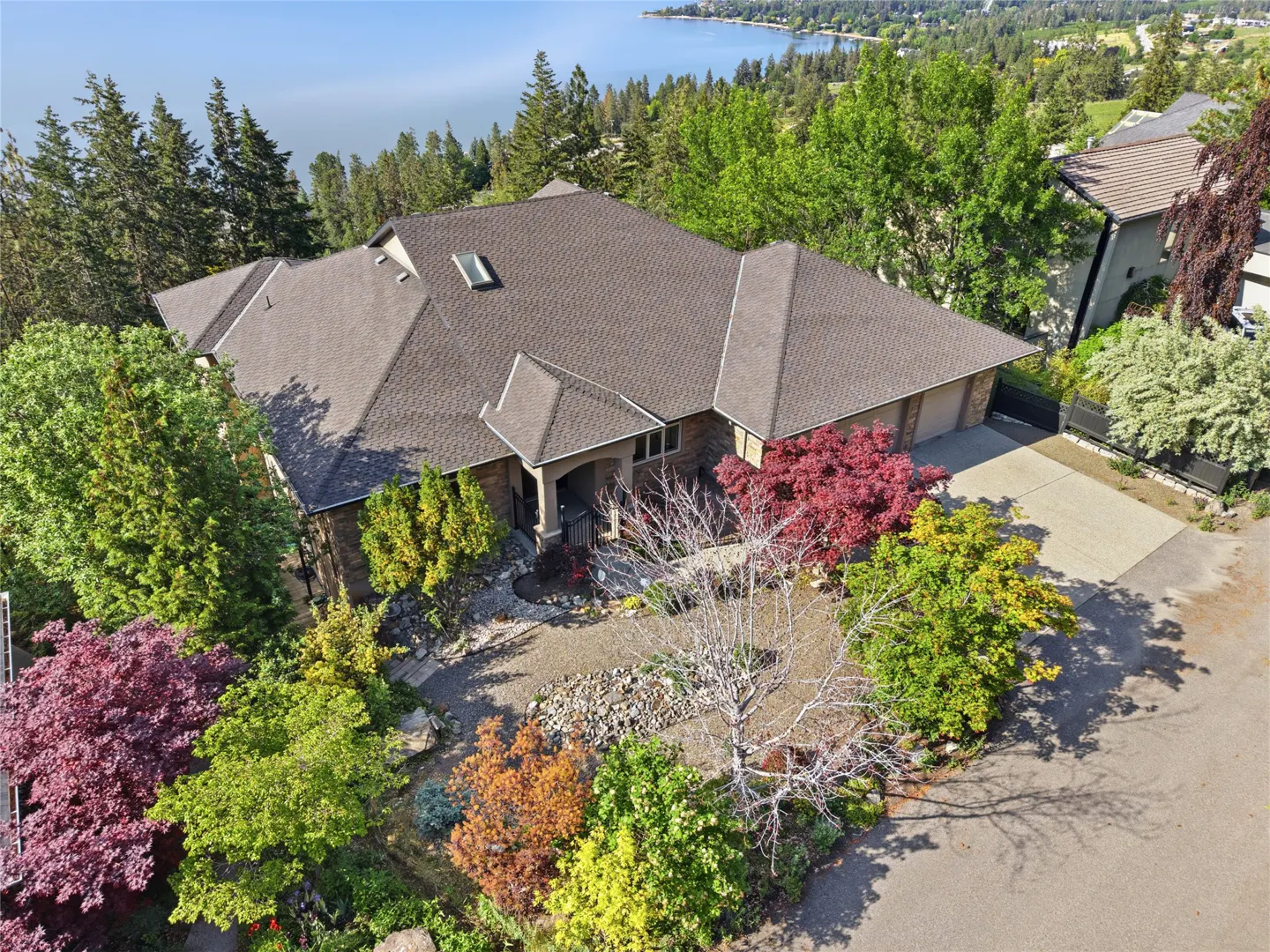 Aerial view of a brown-roofed house surrounded by colorful trees, with a lake and mountains in the background.
