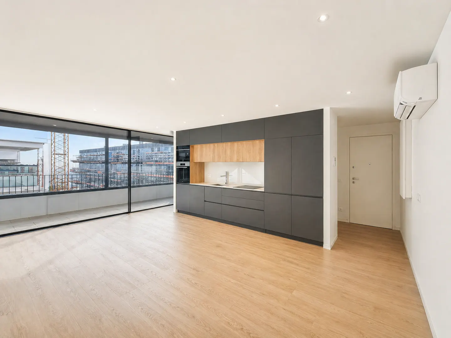 Bright, modern apartment with wood floors, gray cabinets, and a large window overlooking a construction site.